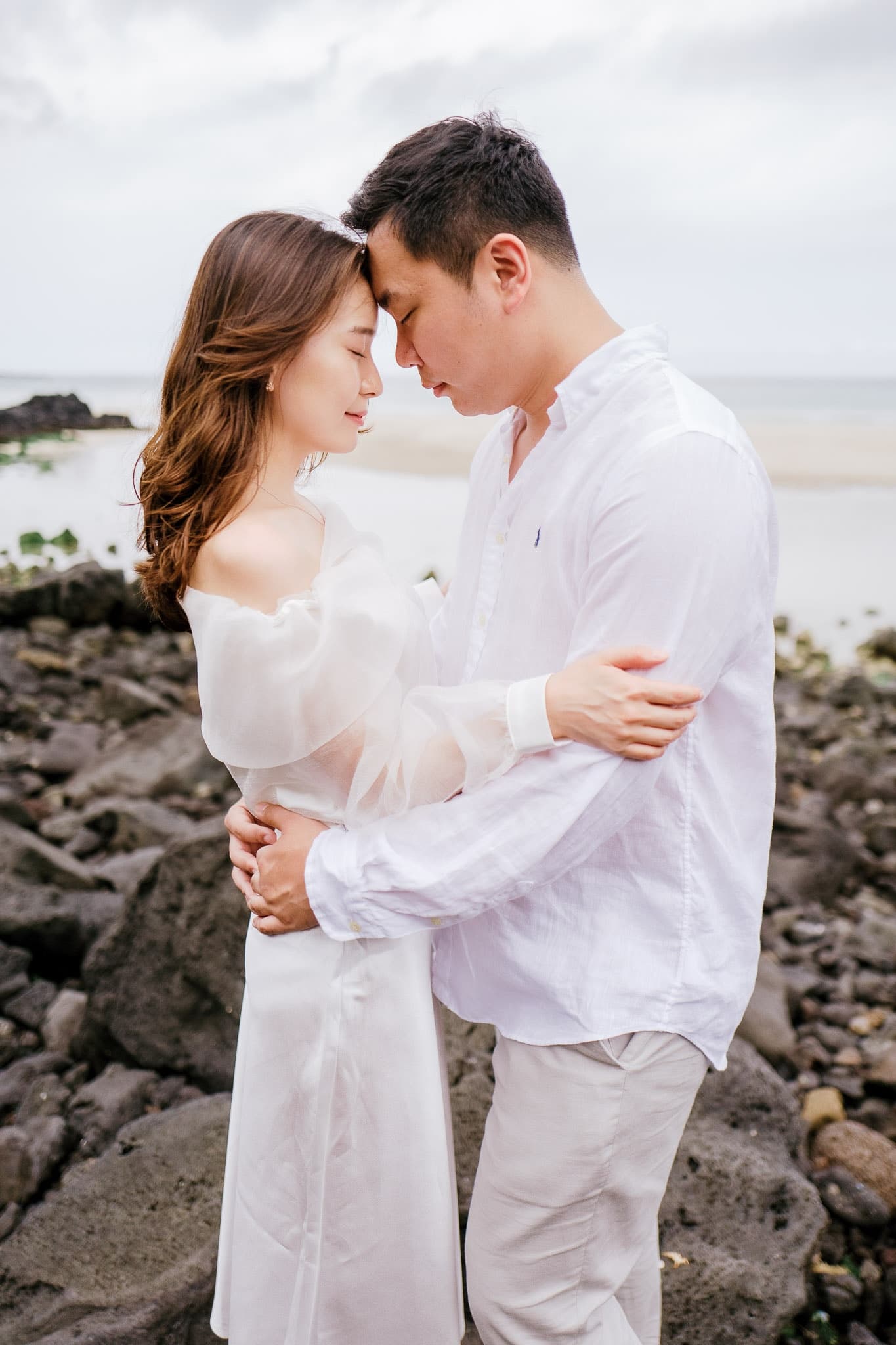 Couple in white touching foreheads on the rocky shore