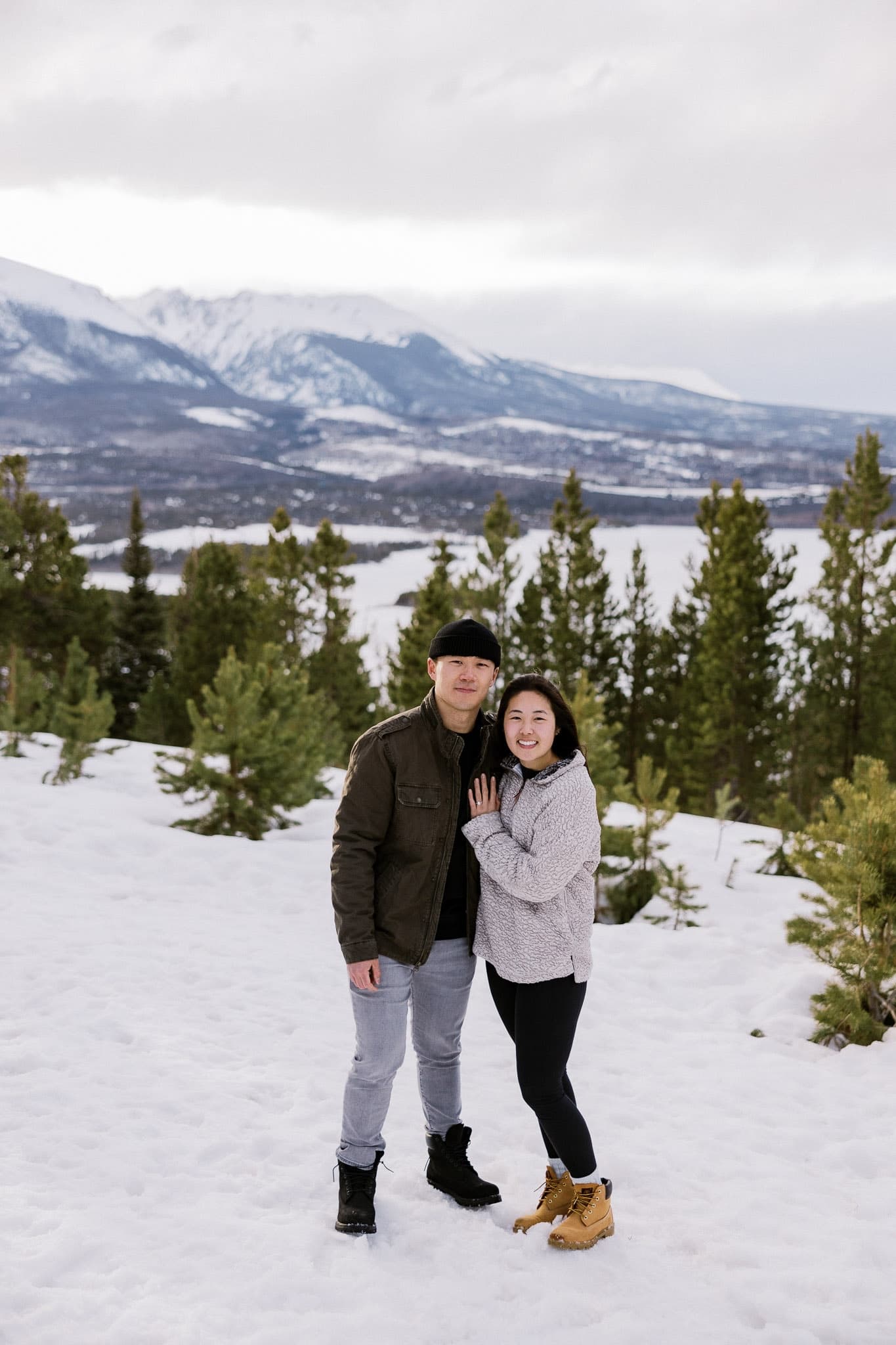 Couple smiling together in the snow among the pines