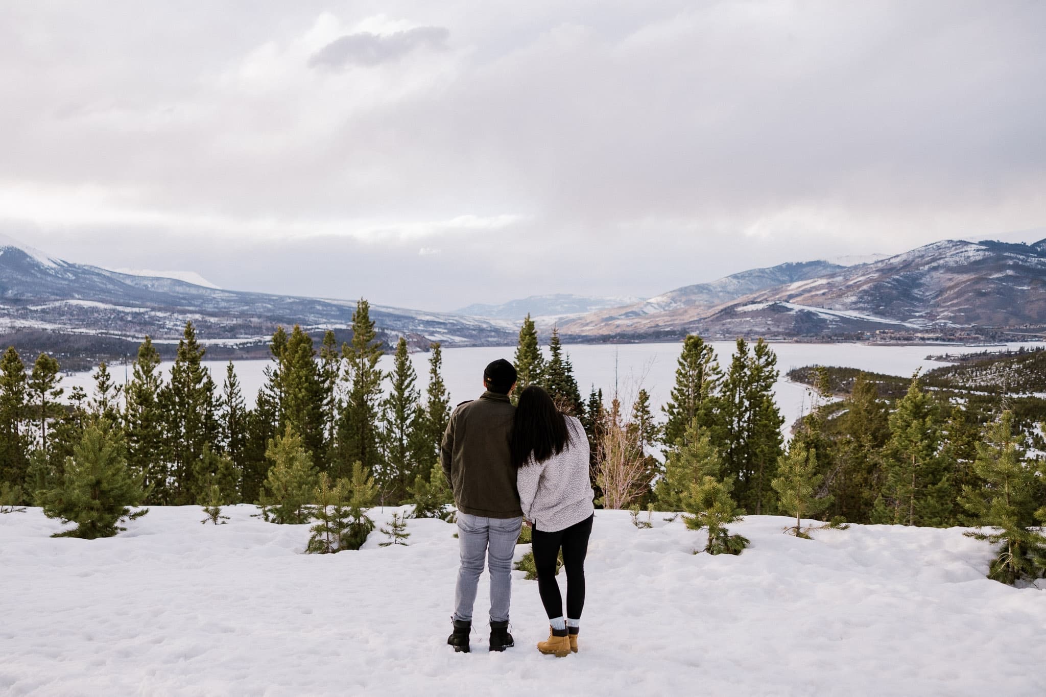 Couple gazing out over the lake and mountains from a snowy overlook