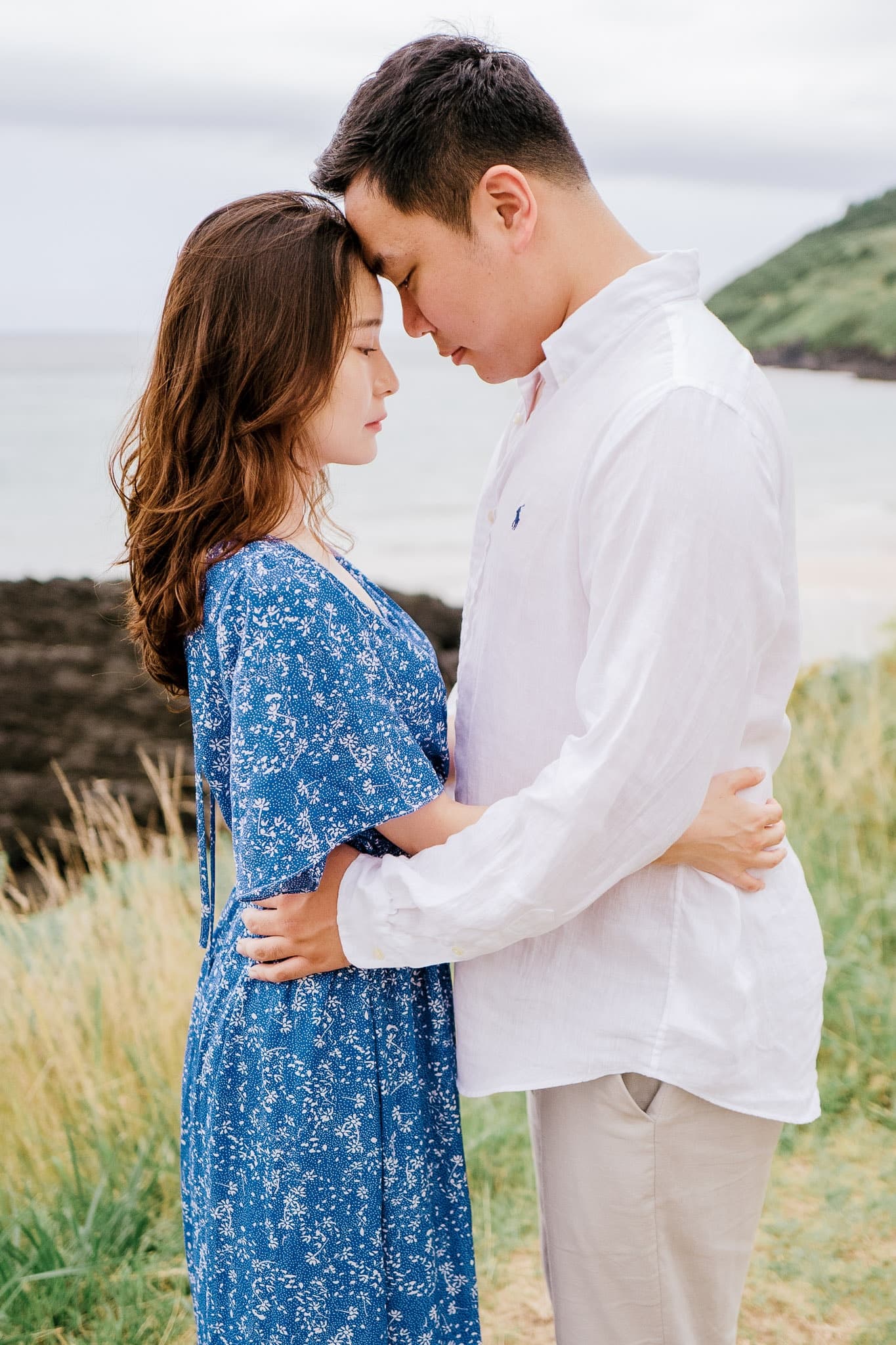 Couple touching foreheads on a grassy bluff by the sea