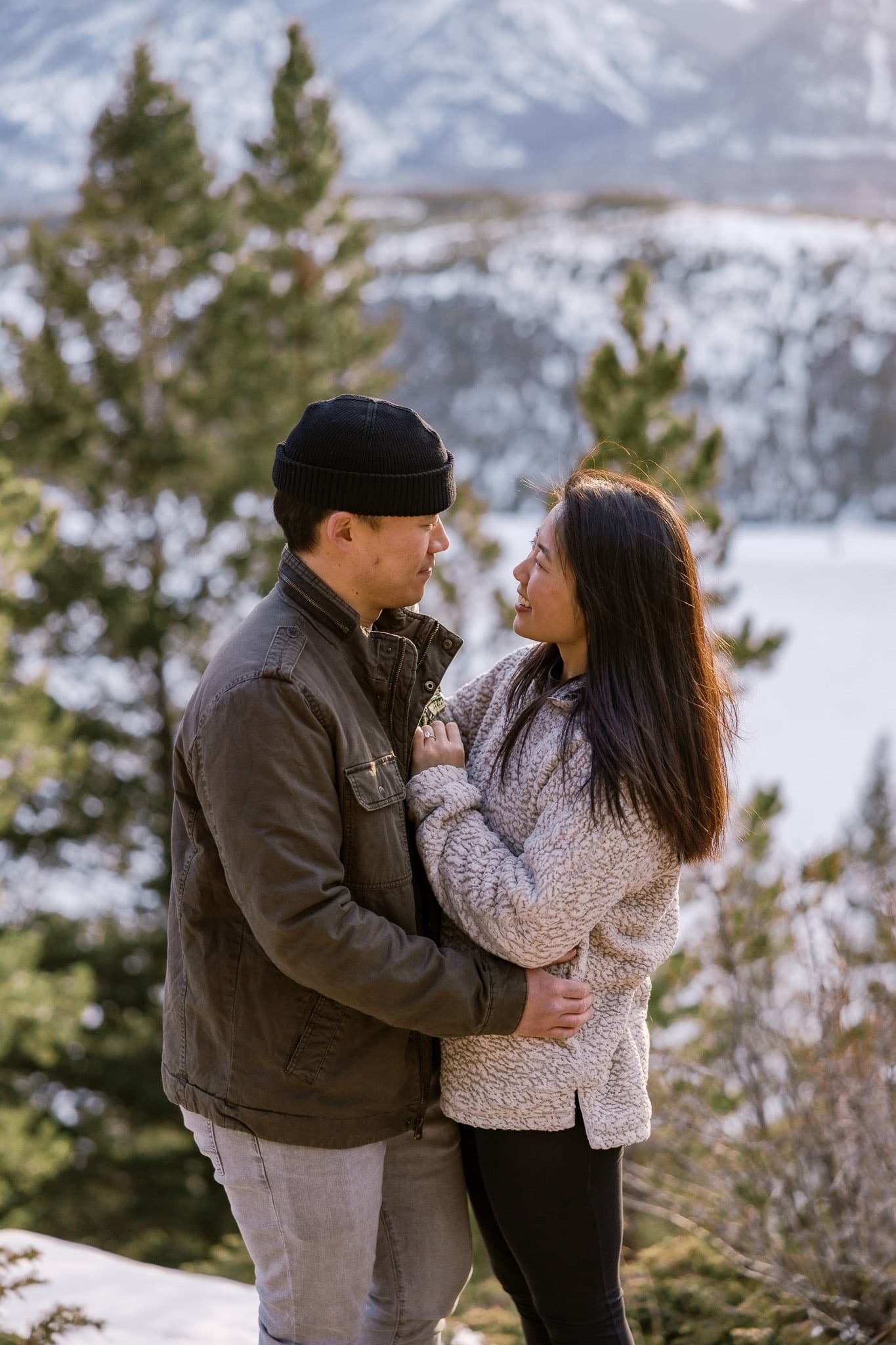 Couple holding each other among the pines in the snow