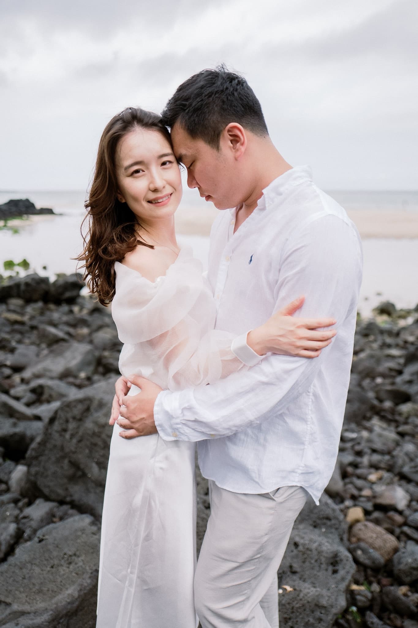Couple in white smiling together on the rocky shore