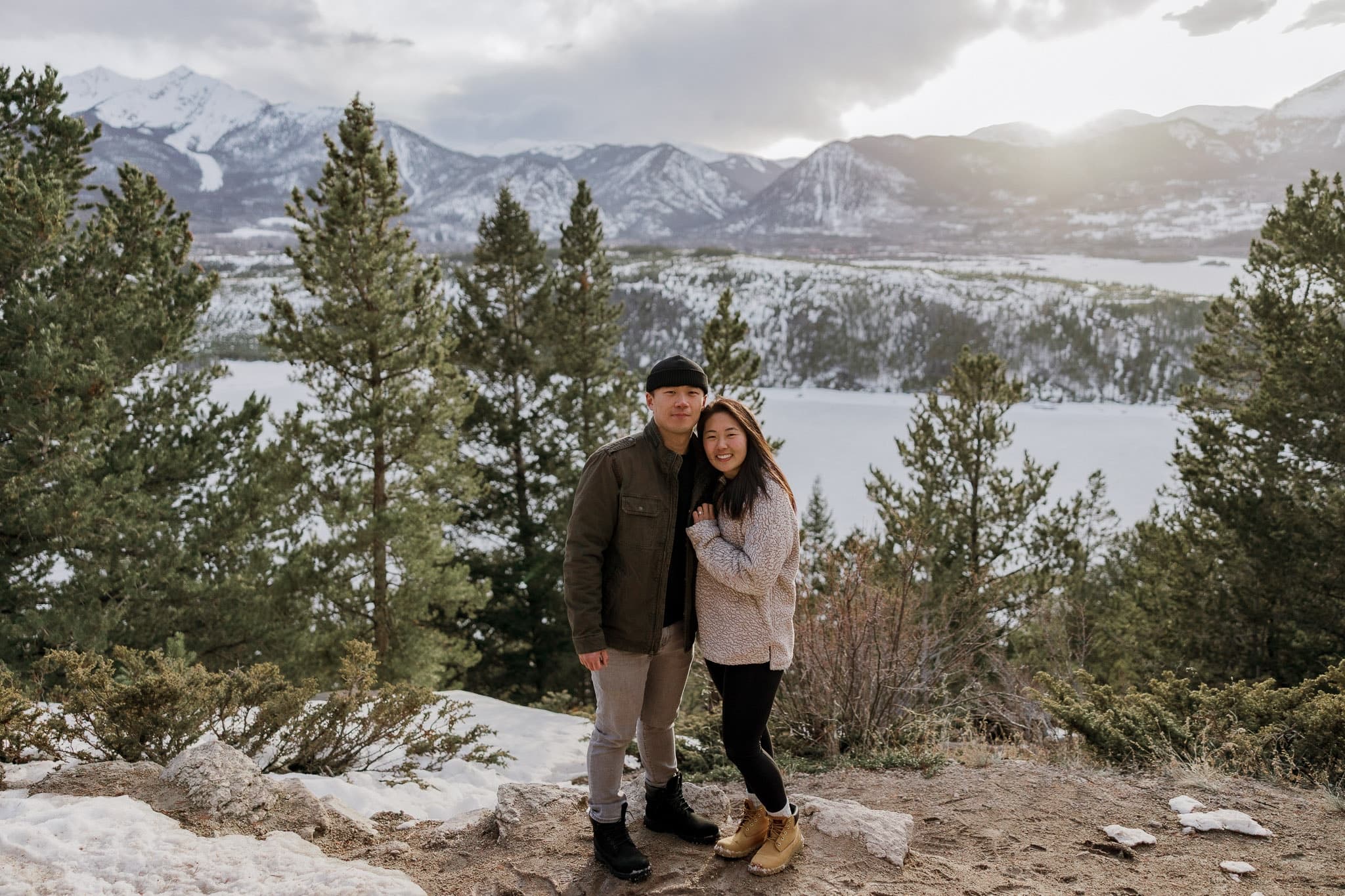 Couple on a snowy overlook with the sun breaking over the mountains