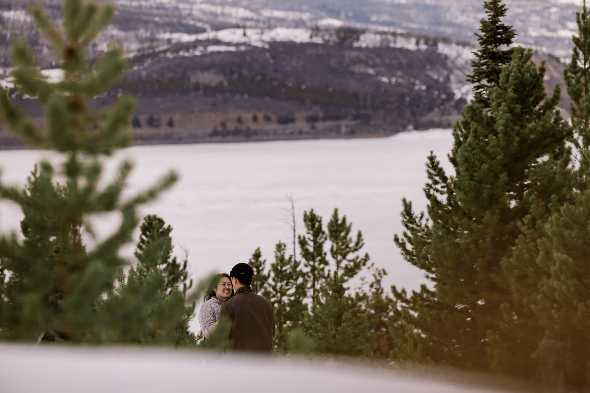 Couple glimpsed through the pines above a mountain lake