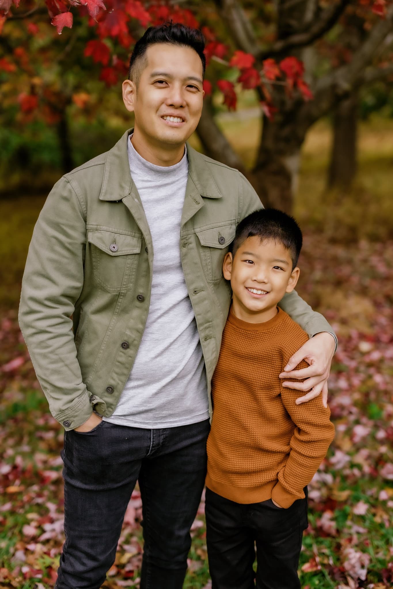 Parent and child posing together under red autumn leaves