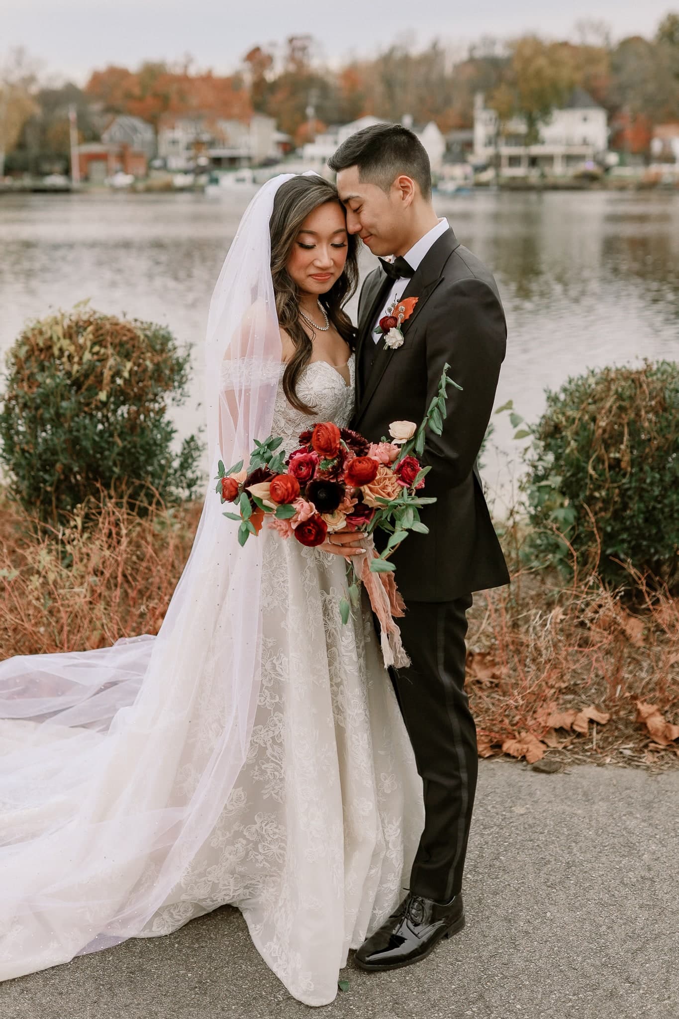 Couple embracing by the lake with a bouquet of deep red flowers