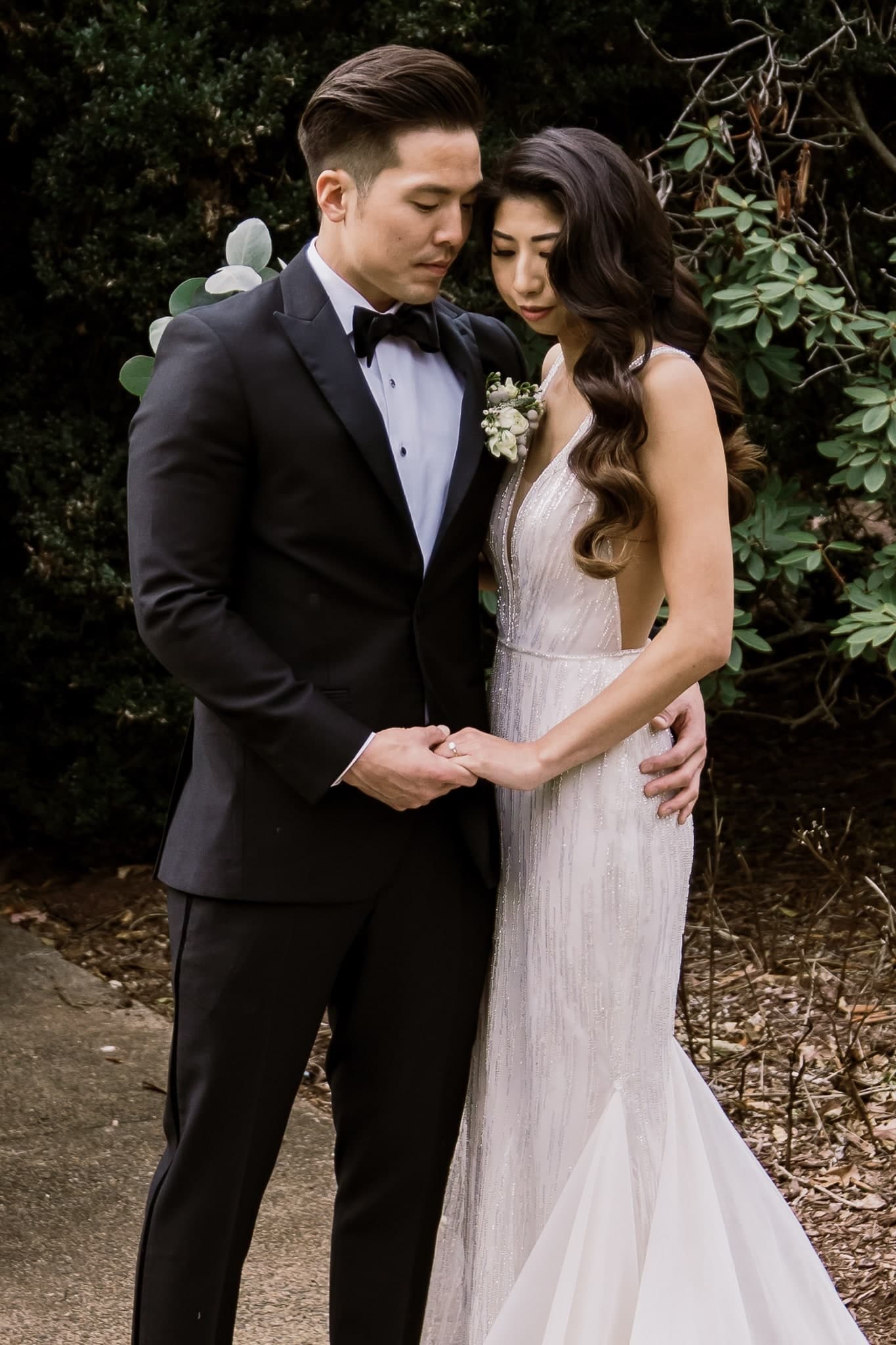 Couple holding each other close in front of evergreen hedges