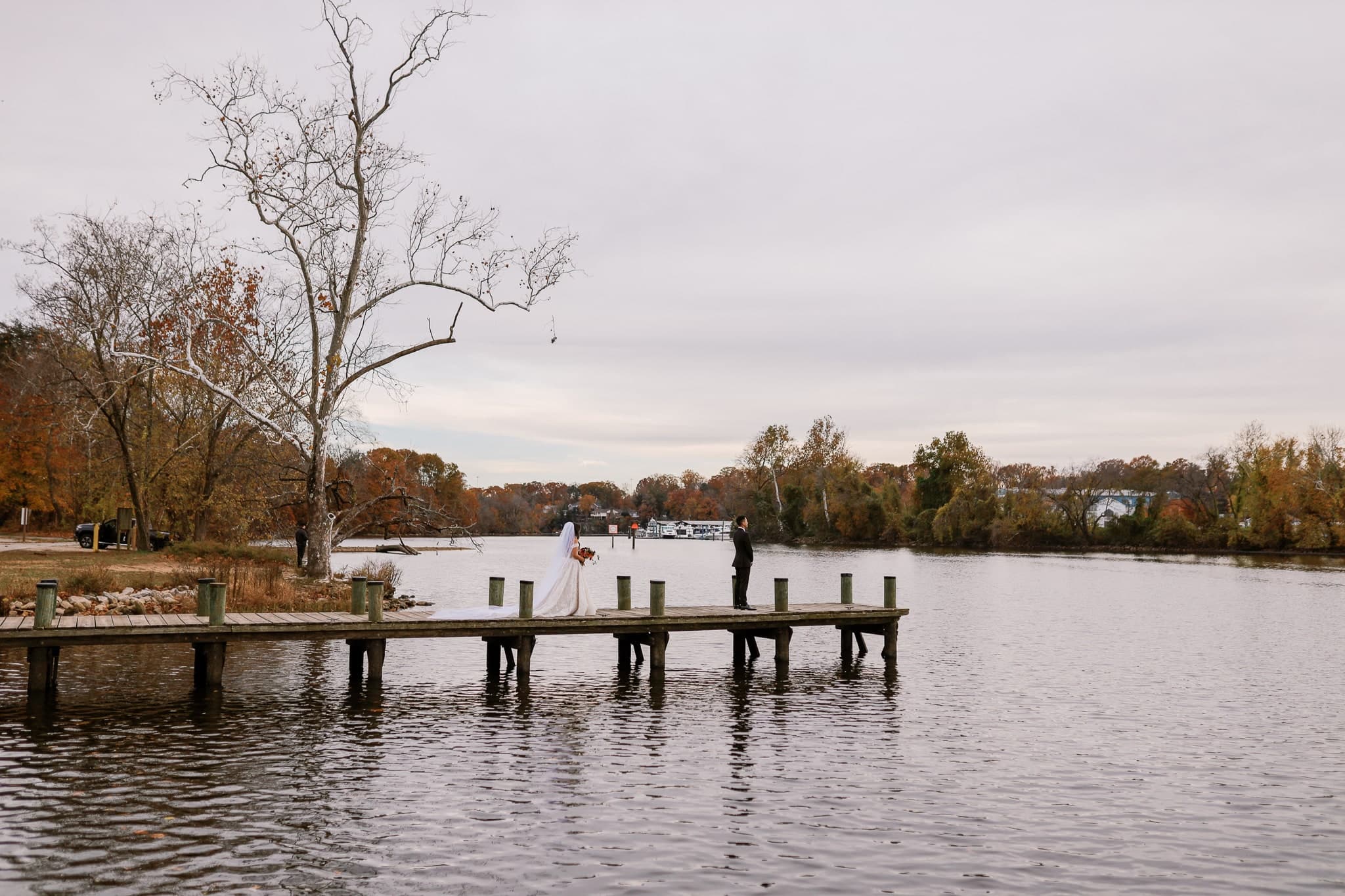 First look on a lakeside dock, the bride approaching as the groom waits