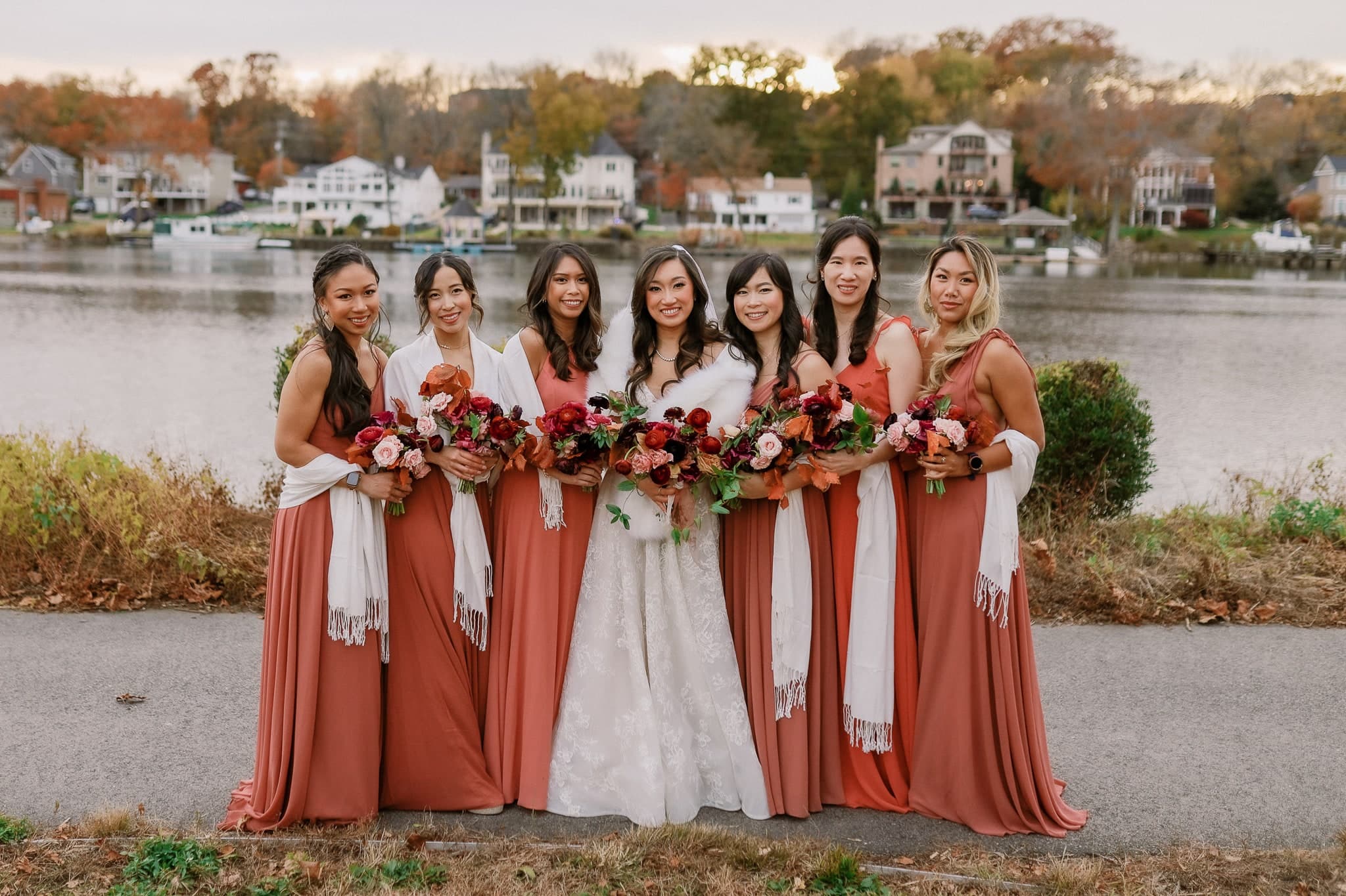 Bridesmaids in rust gowns with the bride by the lake