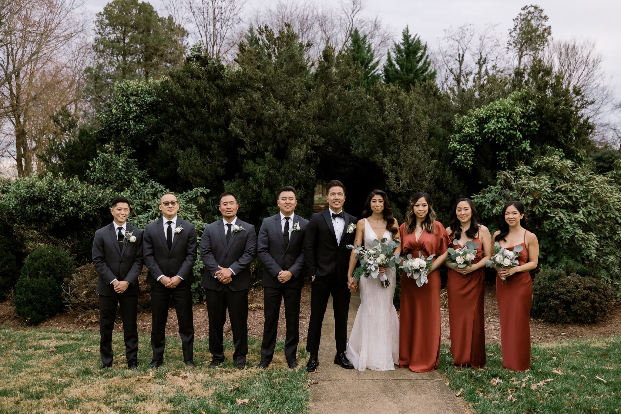 Wedding party lined up in front of evergreen hedges
