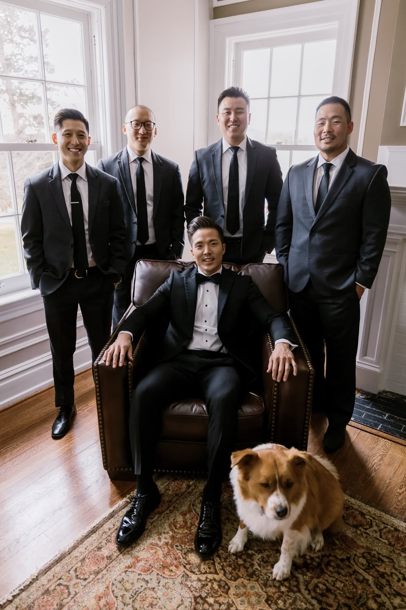 Groomsmen gathered around the groom and a corgi