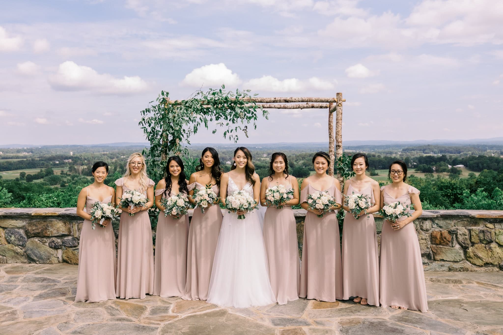 Bridesmaids in blush gowns at the hilltop arbor