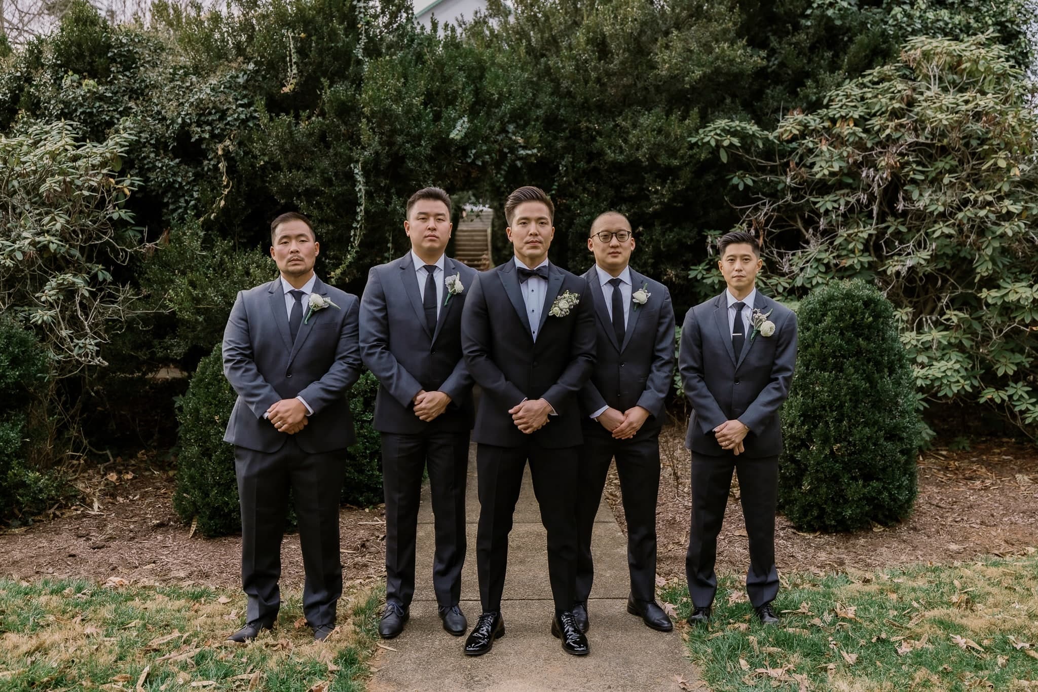 Groomsmen in navy suits in front of the hedges