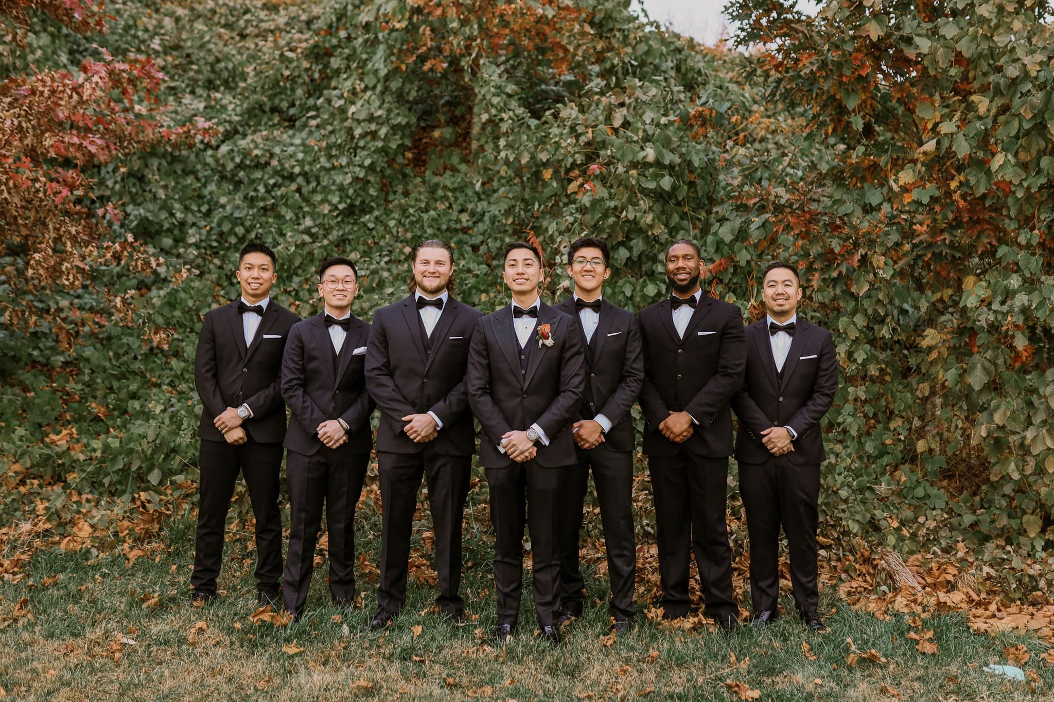 Groomsmen in tuxedos against an ivy wall