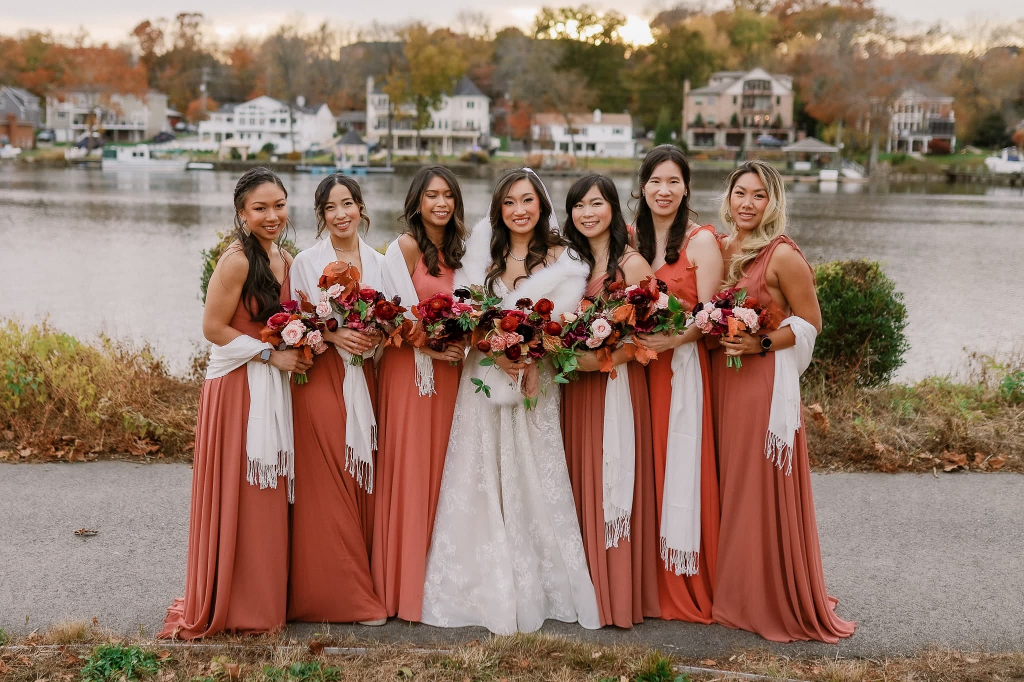 Bridesmaids holding red bouquets by the lake
