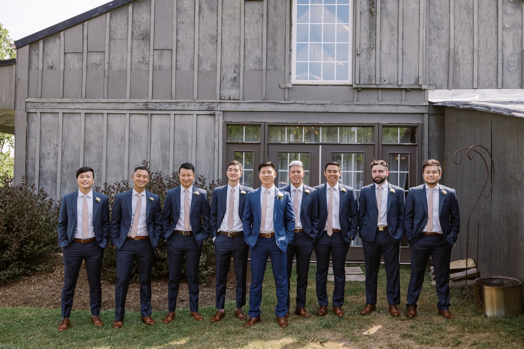 Groomsmen lined up in front of a weathered barn