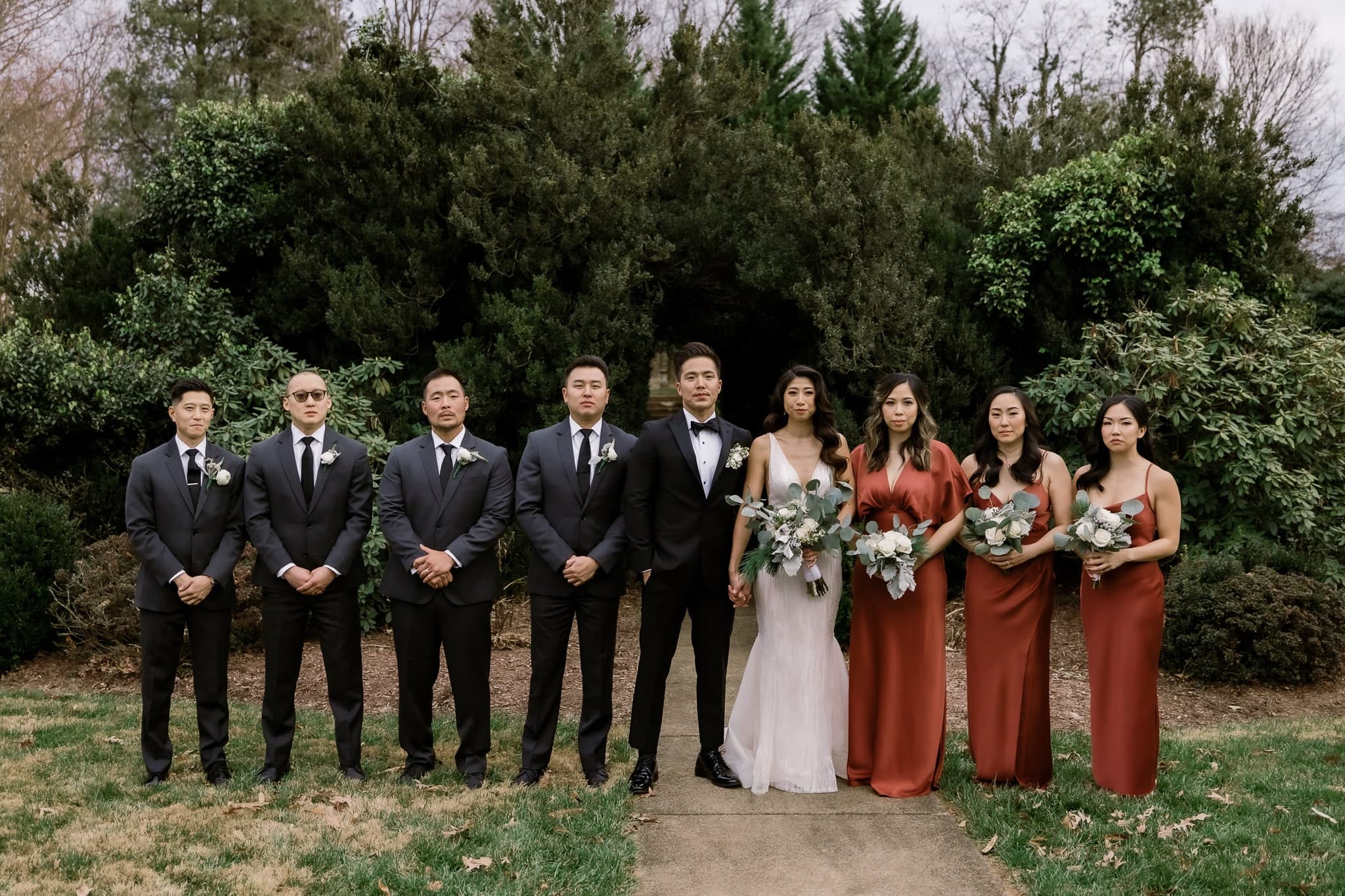 Wedding party posed in front of evergreen hedges