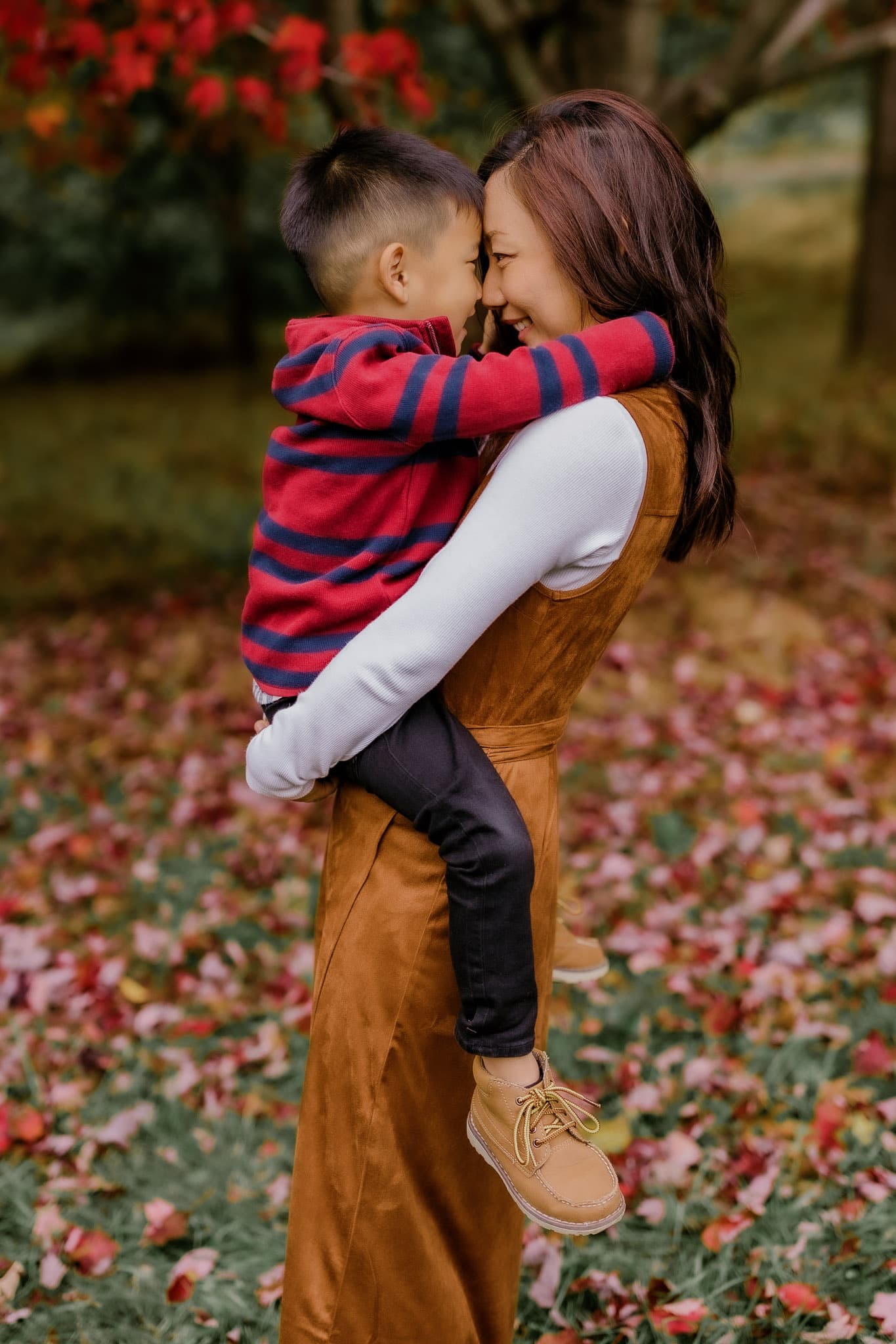 Parent hugging a young child in front of a red maple